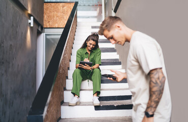 Woman sitting and drawing with stylus on tablet while smiling at man, showing open collaboration,...