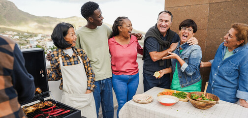 Multigenerational people doing barbecue at home's rooftop - Multiracial friends having fun eating and cooking together during weekend day - Summer and food concept - Main focus on african woman face