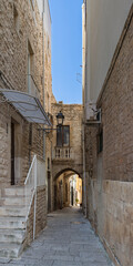 A quaint alley in the historic center of Palo del Colle, Italy. Stone walls, lantern, and archway evoke Mediterranean charm under a vivid blue sky and timeless architecture.