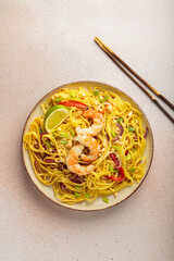 Delicious pad thai dish with shrimps, peanuts, lime and chopped vegetables, chopsticks on light...