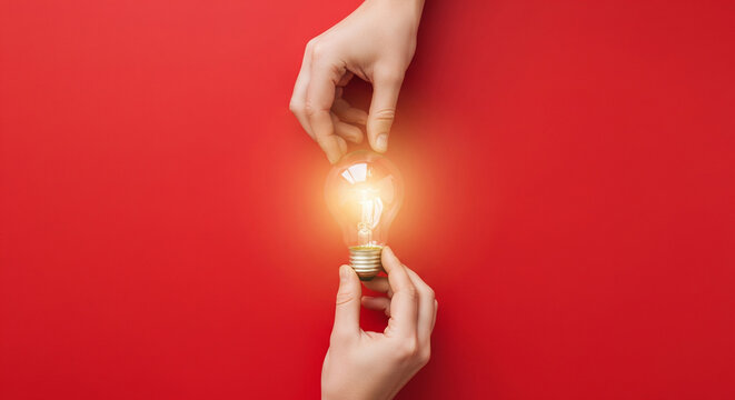 Two hands holding a glowing light bulb against a vibrant red background, symbolizing the generation of new ideas, innovation, and creative thinking