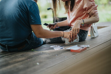 A close-up view showcases two individuals playing cards outdoors, surrounded by natural light. Their casual posture expresses relaxation and enjoyment of leisure time.
