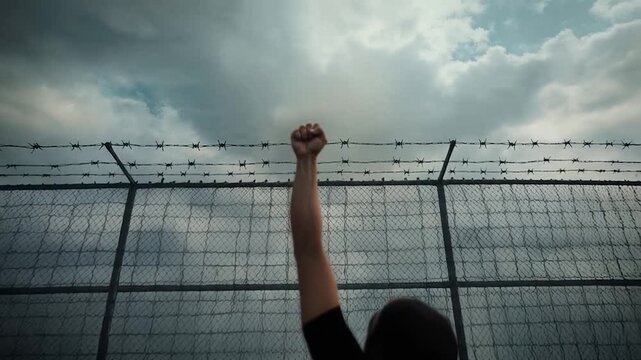 Powerful Symbol of Resistance &ndash; Clenched Fist Under Cloudy Skies with Barbed Wire and Atmospheric Dust


