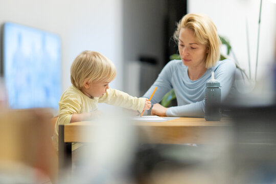 Caring young Caucasian mother and small son drawing painting in notebook at home together. Loving mom or nanny having fun learning and playing with her little 1,5 year old infant baby boy child