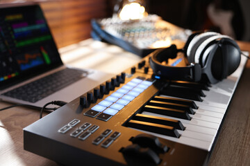 MIDI keyboard with headphones, laptop and dj mixer on wooden table indoors, closeup