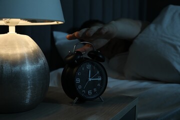 Man suffering from insomnia in bed indoors, focus on alarm clock