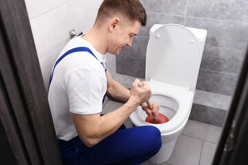 Plumber unclogging toilet with hand plunger indoors