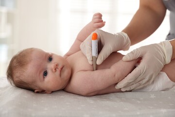 Pediatrician examining baby with thermometer at table in clinic, closeup