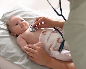 Pediatrician examining baby with stethoscope at table in clinic, closeup