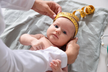Pediatrician measuring baby's head with tape at table in clinic, closeup