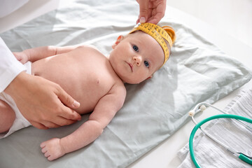 Pediatrician measuring baby's head with tape at table in clinic, closeup