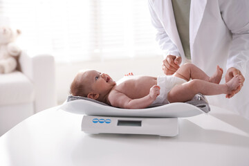 Pediatrician weighting baby with scales at white table in clinic, closeup