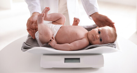 Pediatrician weighting baby with scales at white table in clinic, closeup