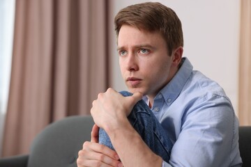 Man suffering from paranoia on sofa at home, space for text