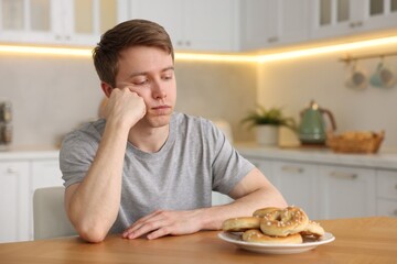 Gluten free diet. Sad woman with pretzels at wooden table in kitchen