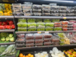 A blurred view of a supermarket aisle, showing shelves filled with fruits and vegetables in plastic containers.