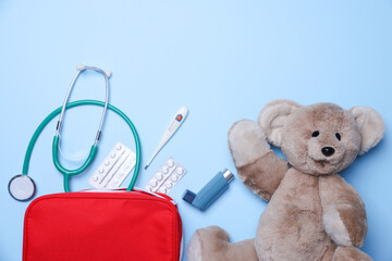 Pediatrics concept. Toy bear with stethoscope and first aid kit on light blue background, flat lay