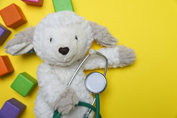 Pediatrics concept. Toy sheep with stethoscope and cubes on yellow background, top view