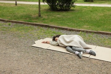 Homeless woman sleeping on carton in park, space for text