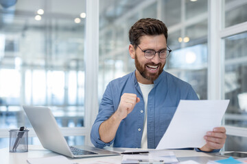 A man in glasses is smiling and holding a paper, as if he has achieved a success in the office.