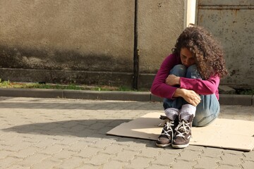 Homeless woman sitting on carton outdoors, space for text