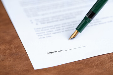 Signing notary document with fountain pen at brown leather surface, closeup