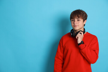 Cute teenage boy with headphones on light blue background. Space for text