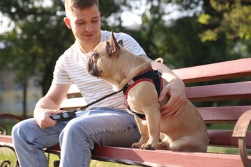 Happy man with his cute French bulldog on bench in park