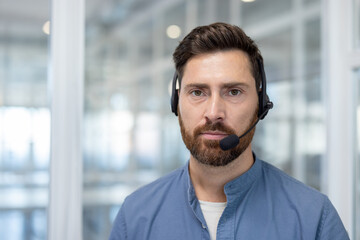 A close-up shot of a man wearing a headset, looking directly at the camera. He has a beard and is...