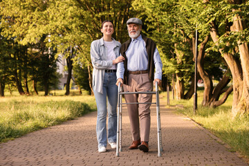 Smiling caregiver supporting elderly man who using walking frame outdoors