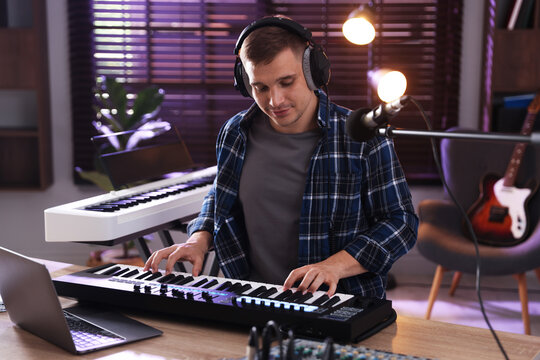 Man in headphones working with MIDI keyboard at table in home studio