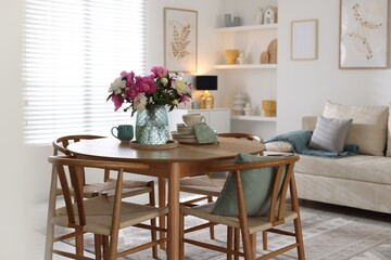 Dining table with beautiful flowers and dishware in room. Interior design