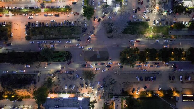 Aerial drone shot straight down into busy roundabout turn with cars passing slowly and being parked at the shopping complexes houses and offices nearby