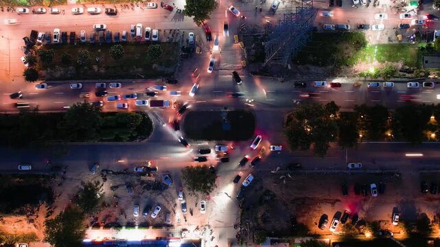Aerial drone hyperlapse shot straight down into a busy roundabout turn with cars passing and parking in nearby markets