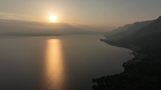 Forward aerial over ocean at sunset with misty Croatian coast, Tucepi village, and mountain layers