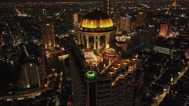 Cinematic drone footage of Bangkok's iconic golden dome building at night, with rooftop bars, river view, and glowing city lights all around.