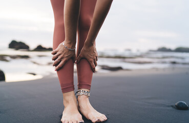 Woman leans forward in standing pose on black beach, hands on shins, barefoot and focused,...