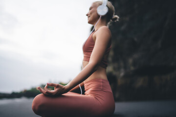 Woman meditates peacefully on black sand with closed eyes and headphones, symbolizing calm...