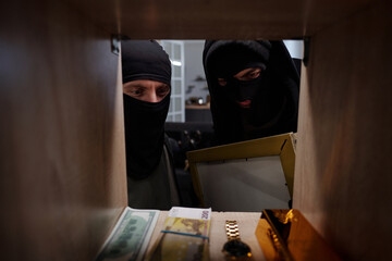 Two men wearing black balaclavas looking into safe, holding box and examining valuables including...