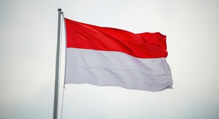 Naklejka premium The red and white flag of Indonesia flutters in the wind against a pale, hazy sky on an overcast day.