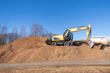 Industrial excavator moving large piles of wood chips under blue sky.