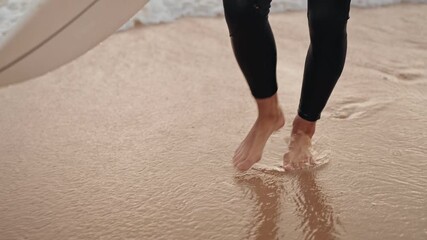 A surfer walks along the beach with their surfboard, enjoying the feeling of sand between their toes.