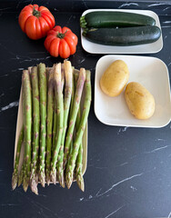 Fresh asparagus, potatoes, tomatoes and zucchinis on black marble countertop
