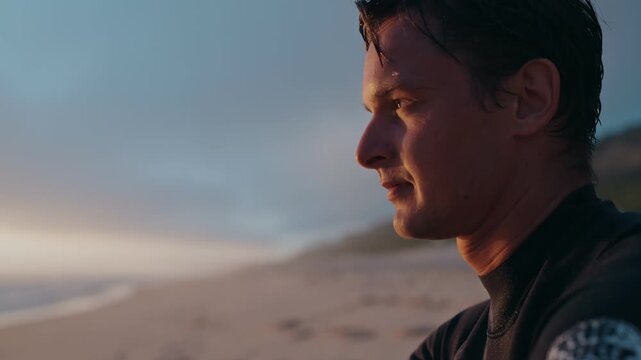 A surfer sits on the beach at sunset, watching the waves and enjoying the peace and quiet.