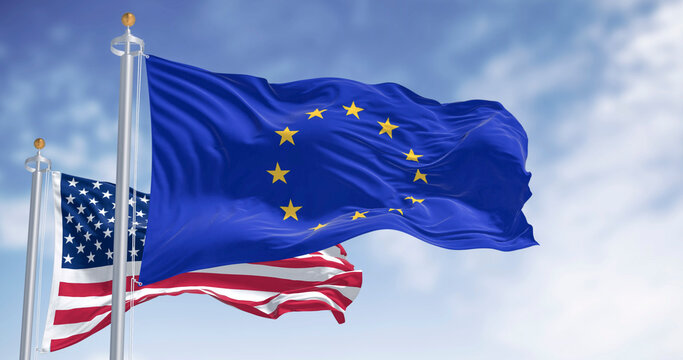 EU and USA flags waving on flagpoles against clear blue sky outdoors