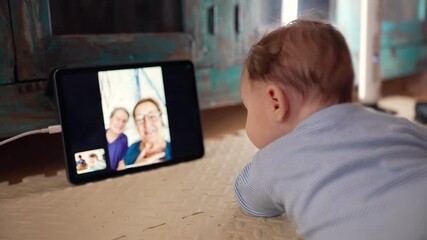 Baby lying on mat engaged with tablet during video call, looking at grandparents on screen, exploring virtual interaction, early exposure to technology and family bonding - Powered by Adobe