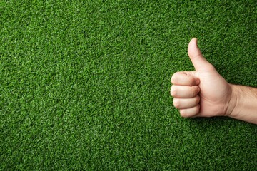 A hand giving a thumbsup on green grass or synthetic turf
