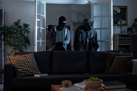 Two men wearing masks entering living room through open glass doors, holding bags and looking around, and Black men appearing to commit burglary at night