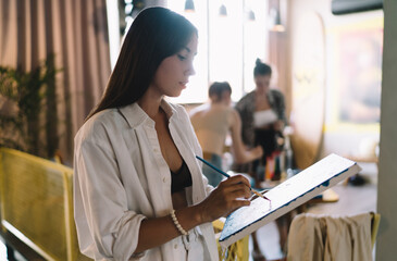 Focused young woman paints standing up during group art session, symbolizing active artistic engagement, independence and creative empowerment through modern artistic tools.