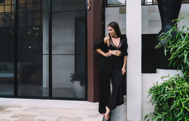 Stylish barefoot woman smiles in front of modern tropical house, expressing freedom, joy and...